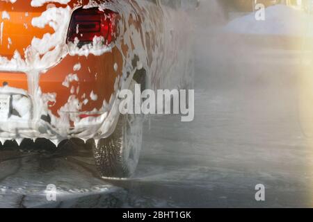 Car is cleaning with soap suds at self-service car wash. White lather on auto. Water splashes around car and soapy water runs down. Stock Photo