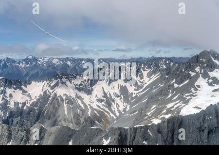 aerial, from a glider, of another glider flying over dark high mountains at Mt. Barth range, shot in bright spring light from west, Otago, South Islan Stock Photo