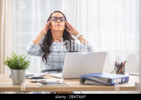 Young woman having eyes closed, fingers on her temples, retrieving mental energy in her work-life balance. Stock Photo