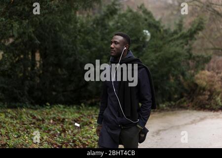 Handsome black man walking through autumnal park wearing headphones. Side view. Stock Photo