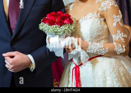 Bride and groom holding bridal bouquet close up . Red roses in brides hands . Stock Photo
