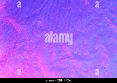 Background from purple recyclable polyethylene in neon pink light. Eco, zero waste, alternative to plastic concept. Flat lay. Horizontal. Closeup. Stock Photo
