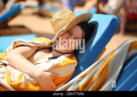 Portrait of a beautiful caucasian woman in 30s lying on the beach sun lounger and hiding from the sun behind the straw hat Stock Photo