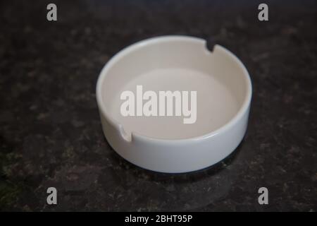 Close up, selective focus, shallow depth of view. Round glass ashtray isolated on black background . Clean empty round white glass ashtray on an old Stock Photo