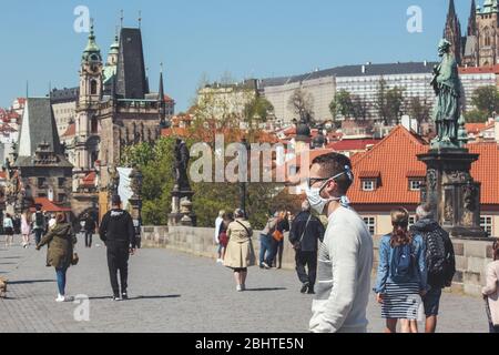 Prague, Czech Republic - April 23, 2020: People wearing medical face masks on the Charles Bridge. Old town in background. City center during coronavirus pandemic. COVID-19 crisis. Horizontal photo.
