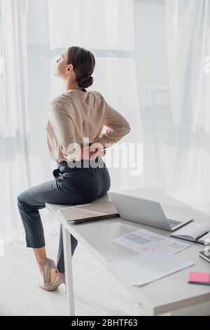 tired businesswoman stretching back on workplace with laptop Stock Photo