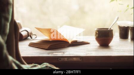 Cup of coffee and an open old book on a wooden windowsill. Retro style Stock Photo