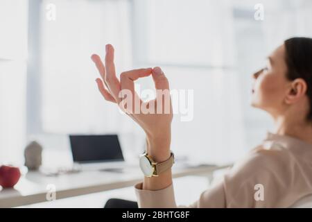 selective focus of businesswoman meditating with gyan mudra at workplace Stock Photo