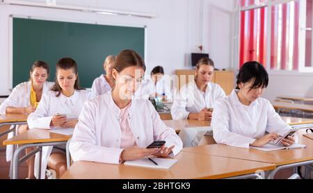Medical students using mobile phones and writing in notepads during lesson Stock Photo