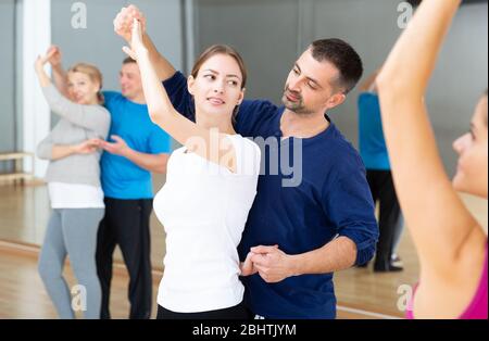 Smiling dancing people practicing bachata movements in dance studio for adults Stock Photo