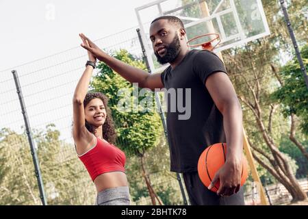 Outdoors Activity. African couple standing on basketball court giving high five smiling happy close-up Stock Photo