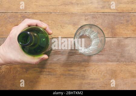 Hand hold bottle on wooen table with glass. Top view. Stock Photo