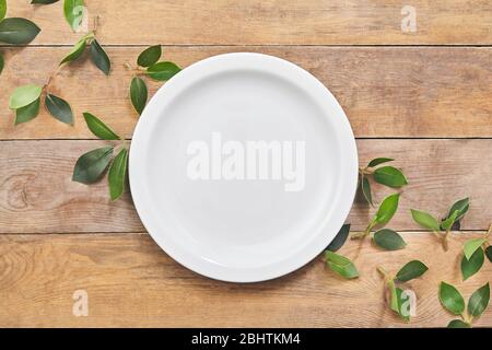 Empty white plate with green leaf on wooden table. Top view. Stock Photo