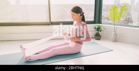 Resistance band home fitness workout woman training with rowing arm exercise using rubber bands on yoga mat floor exercises with strap elastic. Panoramic banner. Stock Photo