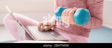 Woman using laptop at home watching fitness videos online workout class training with dumbbell weight. Fit girl using weights working out arms banner panoramic. Stock Photo
