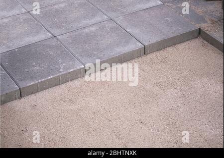 Rows of concrete square pavers or tiles nicely laid in prepared flat sand surface. Still some work is missing. Stock Photo