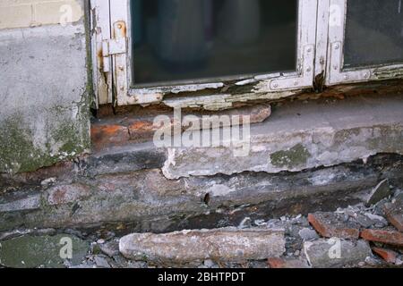 Part of the white wooden frame of an old window with peeling paint and rotten wood and plaster on facade crumbles due to moisture and mold Stock Photo