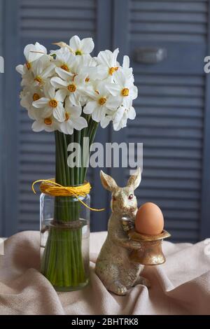Spring composition, golden rabbit figurine with egg and glass vase with daffodils on beige tablecloth, Easter concept, selective focus Stock Photo