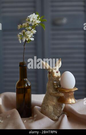 Spring composition, golden rabbit figurine with egg on beige tablecloth and vase with flowering twig, Easter concept, selective focus Stock Photo