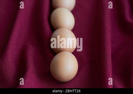 Natural eggs on red tablecloth, several brown chicken eggs lie on burgundy tablecloth, selective focus Stock Photo