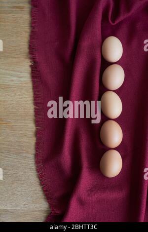 Natural eggs on wooden table, several brown chicken eggs lie on burgundy tablecloth, selective focus Stock Photo