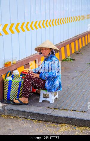 Local lifestyle: a woman wearing a straw conical hat sits with a basket of shopping: street view in Saigon (Ho Chi Minh City), south Vietnam Stock Photo