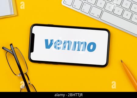 A smartphone showing the Venmo logo rests on a yellow background along with a keyboard, glasses, pen and book (Editorial use only). Stock Photo