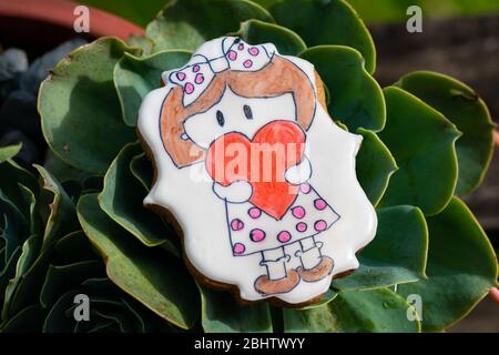Homemade cookie with white icing, with a drawing of a little girl holding a red heart, all hand painted Stock Photo