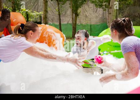 Friendly multiracial team having funny competition in collect of balls in inflatable foam pool on adults bouncy playground Stock Photo