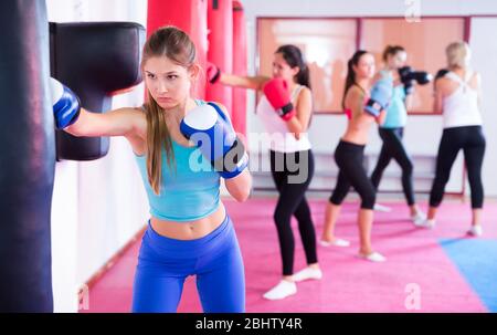 Active adult female is doing exercises with punching bag in sporty gym. Stock Photo