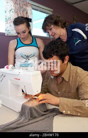 El Paso, Texas.  May 2010: Male Hispanic student at Mission Early College High School learns to use sewing machine in classroom as fellow student and female teacher  look on.  ©Bob Daemmrich Stock Photo