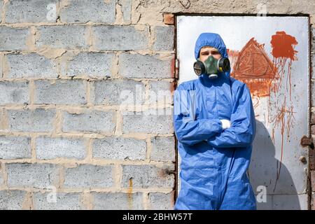 man in protective blue overalls and mask standing near a brick wall, abandoned building. Stock Photo