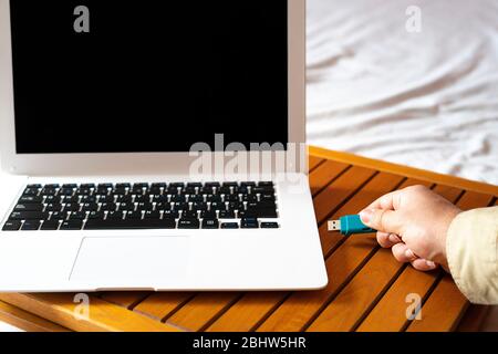 Hand connecting a blue flash drive to a white laptop. Pendrive concept. Stock Photo