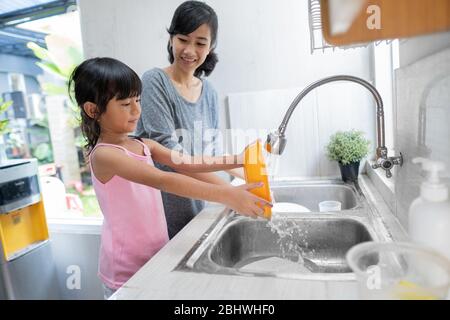 Helping hand. Cute little Girl Help Her Mother In Washing Dishes At Family Kitchen Stock Photo
