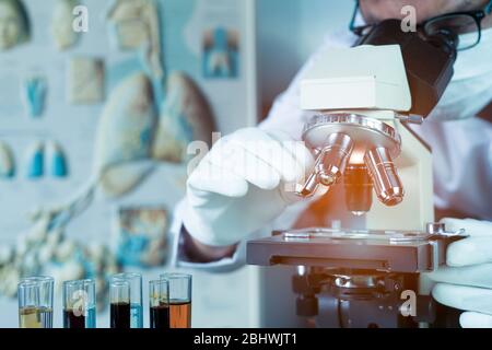Doctor or scientist wear medical face mask and looking in microscope while working on medical research in science laboratory Stock Photo