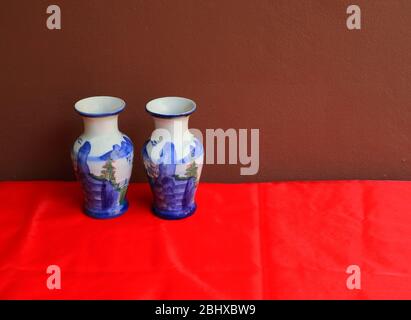 Pair of vintage ceramic vases with chinese landscape painting placed on red creased charmeuse cloth against brown wall, chinese painting is one of the Stock Photo