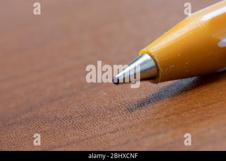 Ballpoint pen nib close-up. It is yellow and brown on the table. Stock Photo