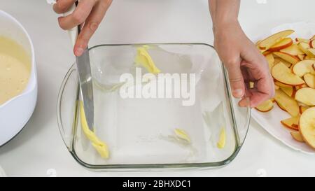 Biscuit batter preparation process. Woman spreads butter and flour over the sides of glass baking form. Stock Photo