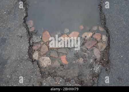 Pot hole revealing old stone road below modern asphalt. Stock Photo