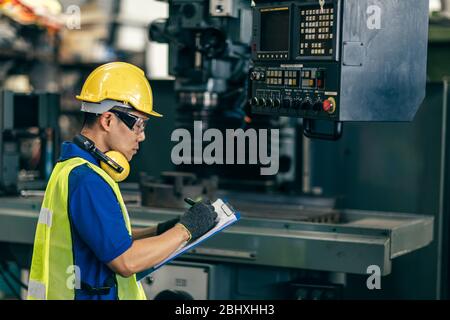Asian engineer checking the machine in factory, worker writing note with list paper. Stock Photo