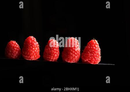 Fresh raspberries on a knife blade isolated on a black background Stock Photo