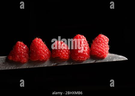 Fresh raspberries on a knife blade isolated on a black background Stock Photo