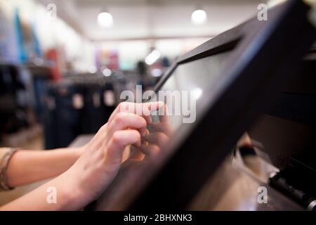 Young woman hand charging a payment for a some clothes by touchscreen treasury at huge shopping centre, finance concept Stock Photo