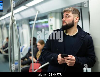 Young focused man browsing and typing messages on phone on way to work in modern metro car Stock Photo