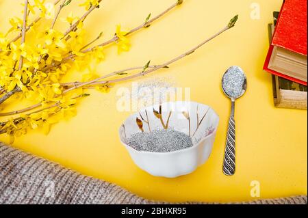 silver glitter spills from a white porcelain mug on a bright yellow background with a silver spoon, a stack of old books, a piece of knitted sweater, Stock Photo