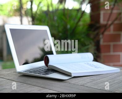 Open book on top of computer laptop. Garden view. Home setting. Onlien education concept. Stock Photo