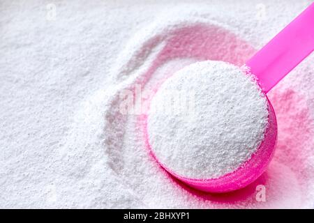 White laundry detergent powder for washing machine and pink plastic scoop for dosage. Image with copy space.