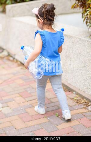 Kid taking out the separate garbage. Back view little girl holding plastic water bottles for recycling. Concept plastic free world the future for our children. Zero waste. Stock Photo
