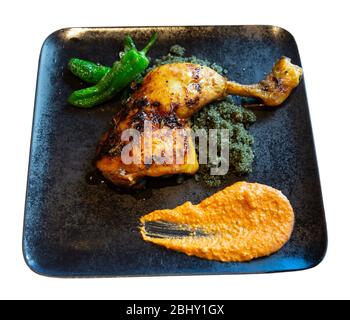 Baked chicken drumstick with garnish of couscous with black curry,  green padron peppers and Romesco. Isolated over white background Stock Photo