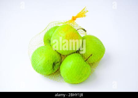 A group of apples in a orange mesh hanging in front of a white wall. Trend. The concept of diet and healthy eating green Granny Smith and golden Stock Photo